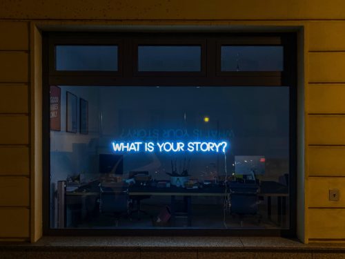 A window with a blue neon side that reads, "What is your story?"