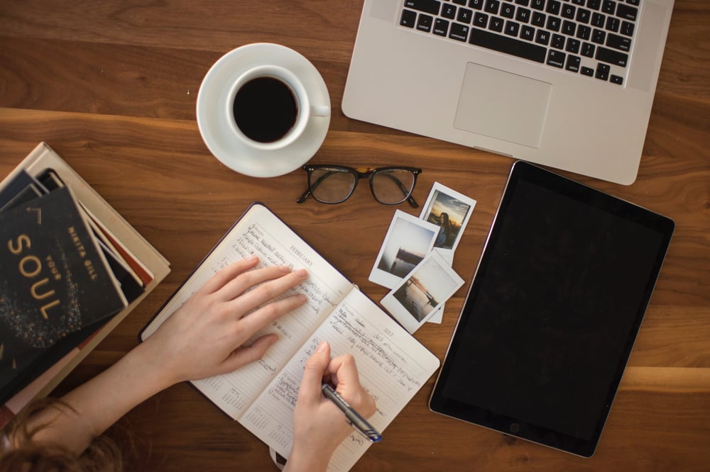 an organized desk with someone writing in a notebook.