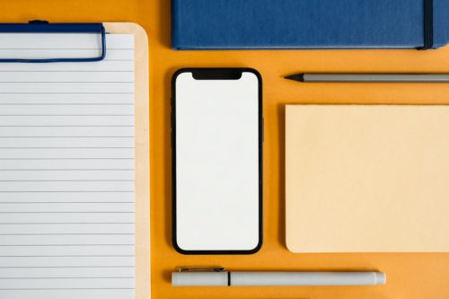 Notepad, smartphone, sticky notes, and pens arranged neatly on an orange surface.