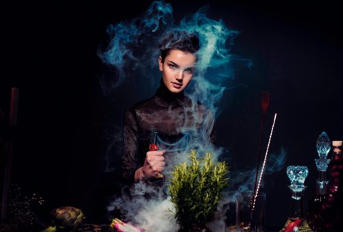 A young witch stirs a potion against a black background.
