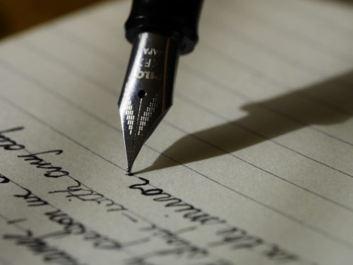 Close-up of a fountain pen writing on a sheet of notebook paper.