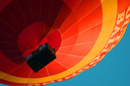 Close-up of the underside and basket of a red, orange, and yellow hot air balloon.