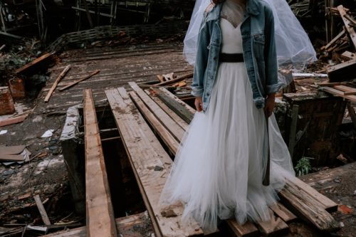 A visual example of how to write exposition using juxtaposition: a person in a wedding gown wears a jean jacket and holds a baseball bat while standing on wooden planks.