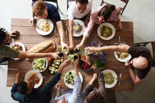 An overhead view of seven friends clinking glasses over a meal.