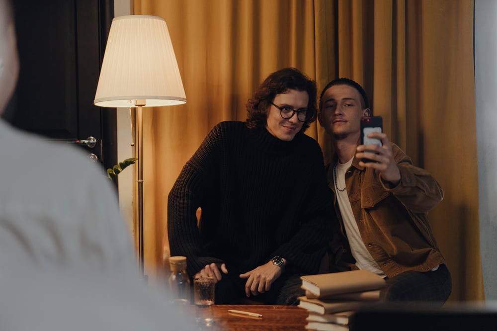 A successful author in a black turtleneck and glasses takes a selfie with a fan.