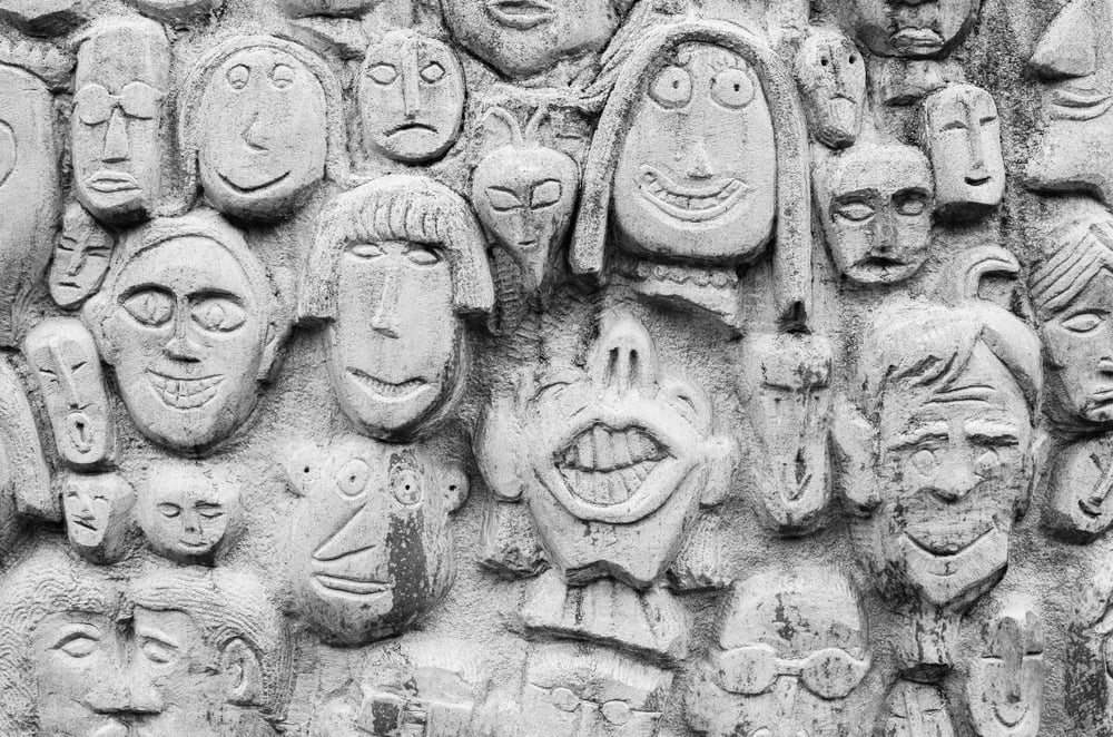 A concrete wall with many cartoonish faces carved into it.