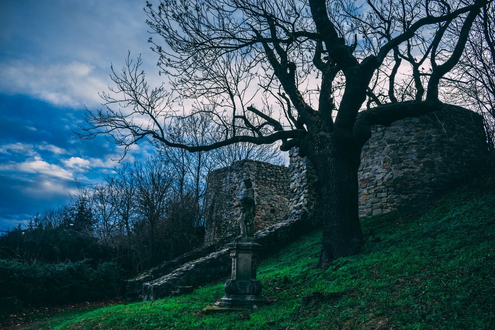 A vibrant green hillside with a dark tree, old statue, and old stone structure.