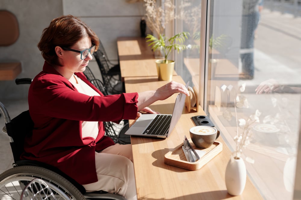 A person in a wheelchair opens a laptop on a table in a cafe.