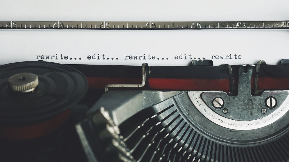 Close-up of a paper in a typewriter with the typed words "rewrite... edit... rewrite... edit... rewrite"