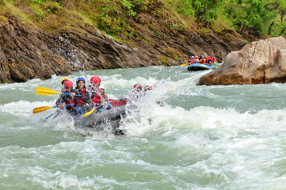 Two groups of people paddle white water rafts through the rapids of a gray-blue river.