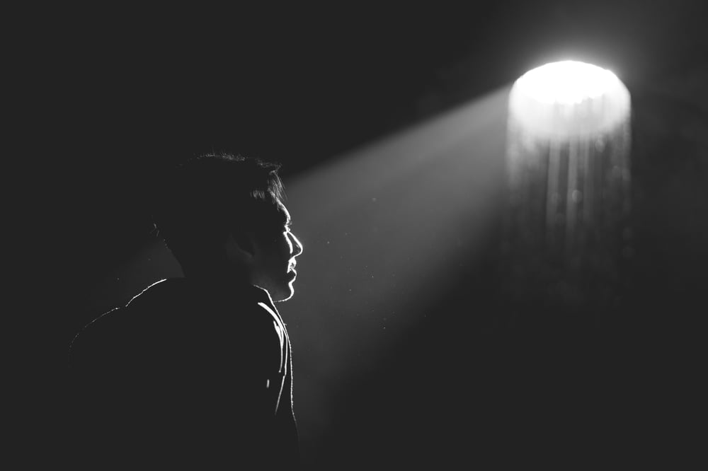 A black-and-white image of a spotlight illuminating the face of a person with short hair.