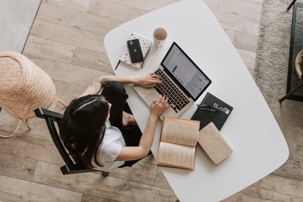 Overhead view of a person typing at a computer with books and notebooks beside them.