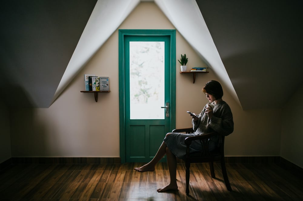 A person sits holding a cup and reading an e-reader beside a green door.