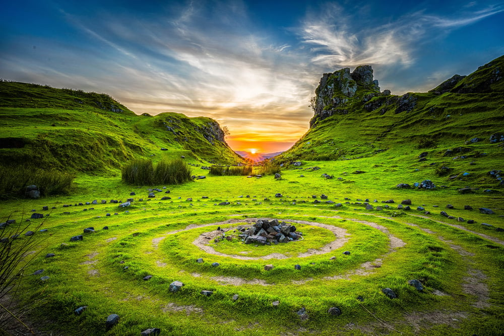 A fantasy world with bright green grass, rocky hillsides, and circular paths.