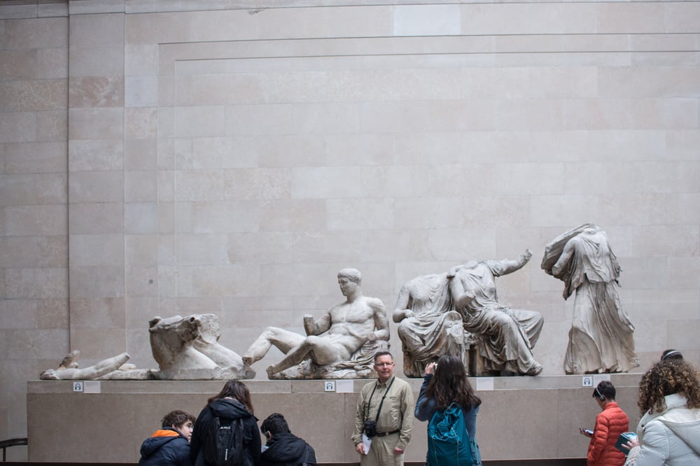 Museum guests take a photo in front of an ancient sculpture.