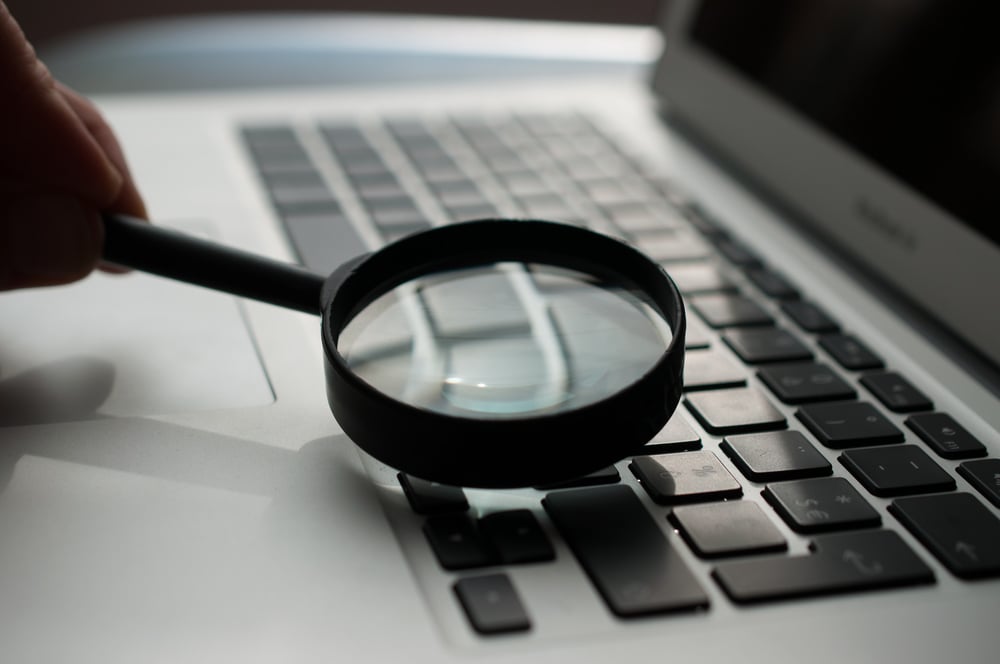 A magnifying glass is held over a computer keyboard.