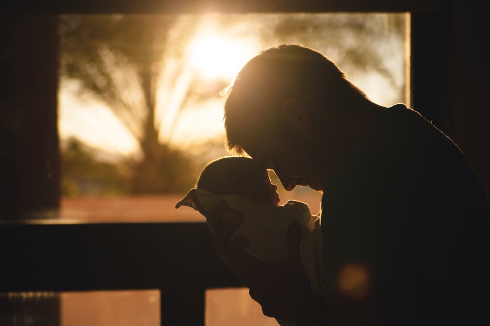 Silhouette of a short-haired parent touching foreheads with their newborn baby.
