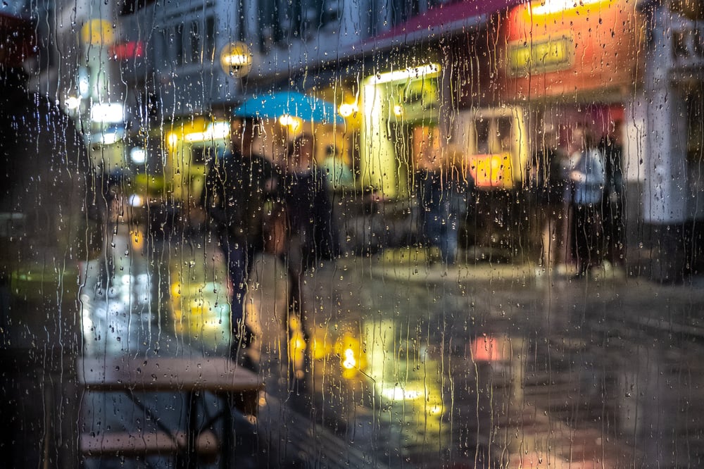 What could you communicate to your reader by showing them your character's blurry view through a rain-streaked window rather than just telling your reader that people walked by in the rain? A view of two people walking down a city street through a rain-streaked window.