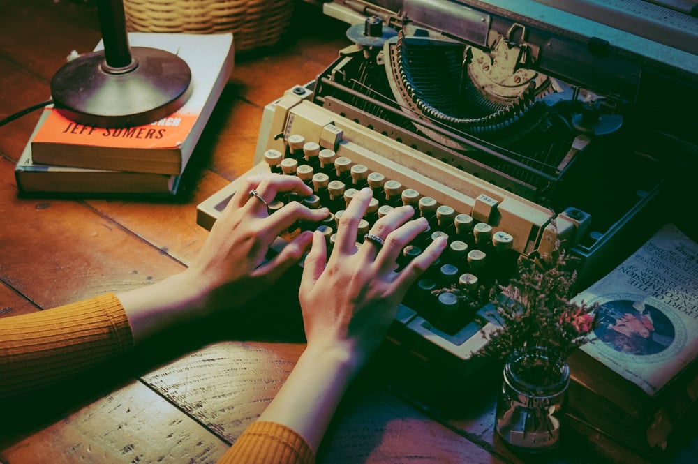 Hands type on an old-fashioned typewriter on a dimly-lit desk.