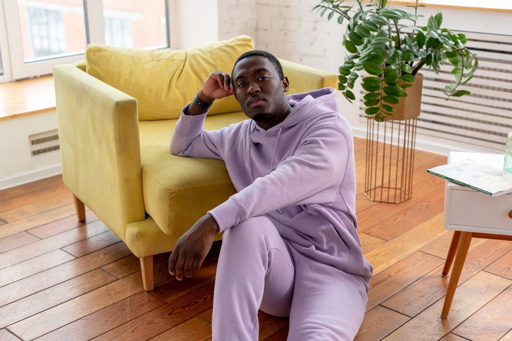 A person in a purple sweat suit sitting on the floor, looking casual, and leaning against a yellow chair.
