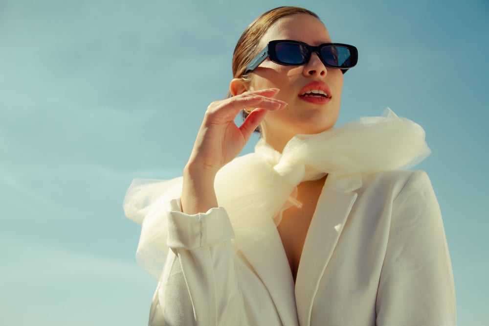 A posh-looking person with sunglasses, a scarf, and hair in a slicked-back bun.