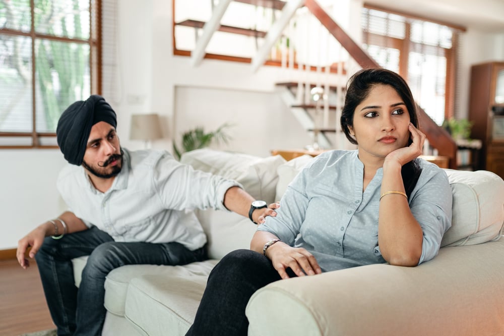 A person reaches across a couch to touch the arm of another person who ignores them.