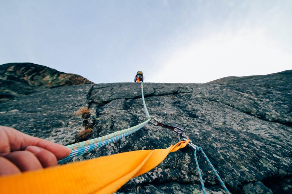 An upward view of a rock climber's hand, rope, and climbing partner.