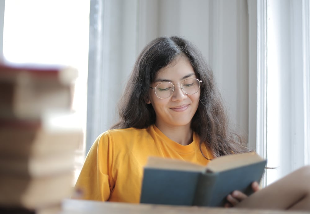A person with long dark hair smiles while reading a book.