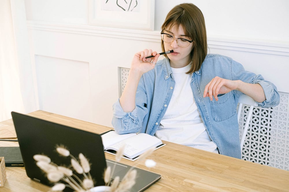 A writer touches a pen to their lips as they look at a computer screen and think.