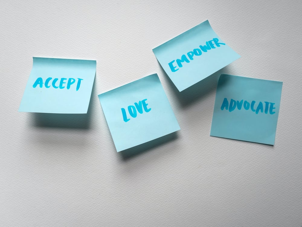 Four blue post-its on a white wall, each reaching "Accept," "Love," "Empower," and "Advocate."