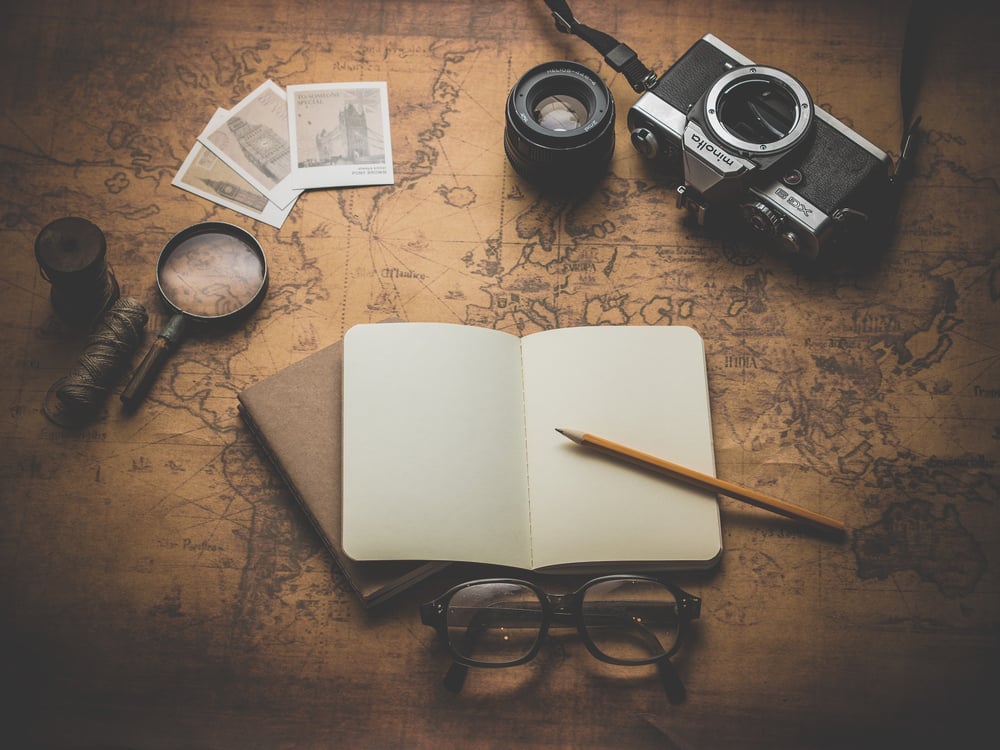 A magnifying glass, notebook, photos, and camera spread out over an old map.