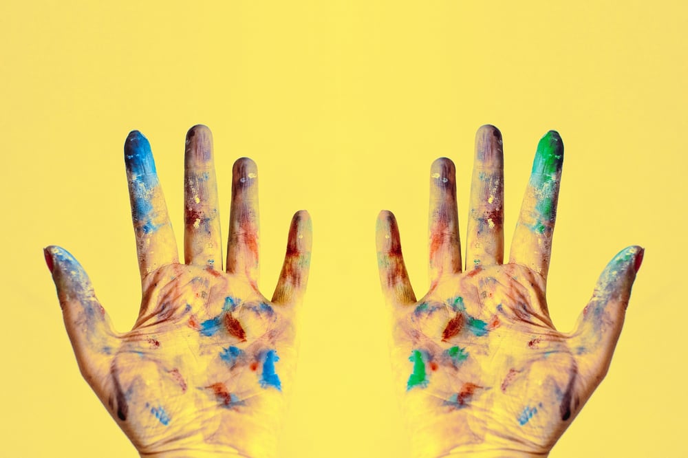 Hands covered in paint against a yellow background.