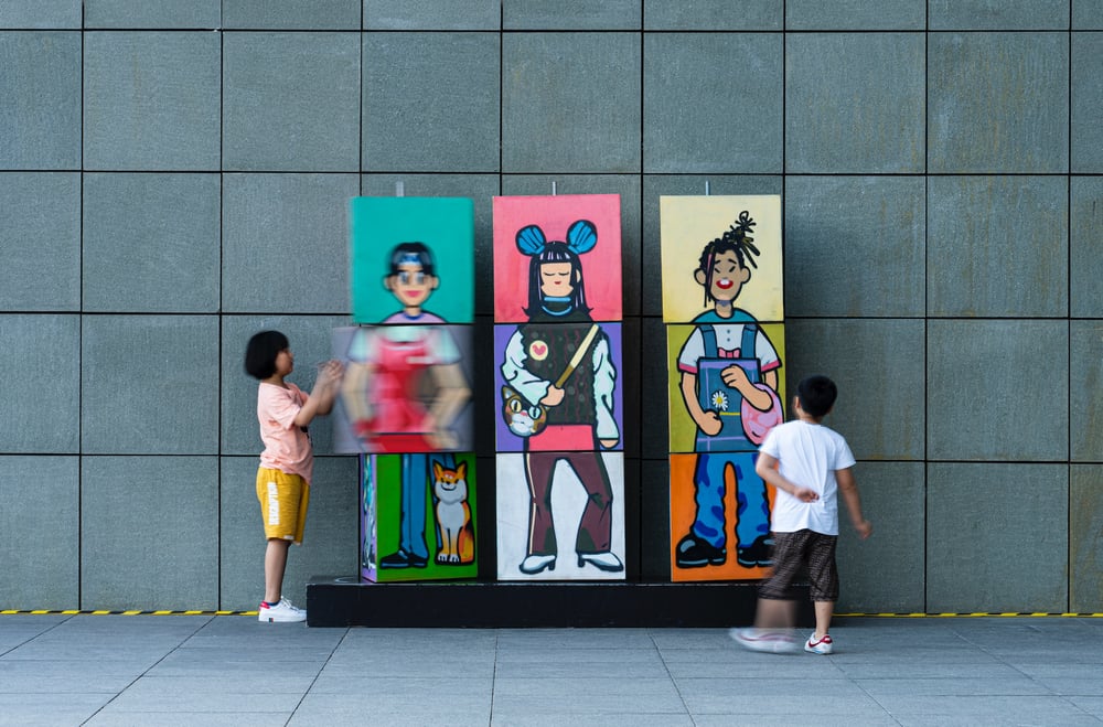 Two children play with an art piece depicting characters with mix-and-match bodies. 