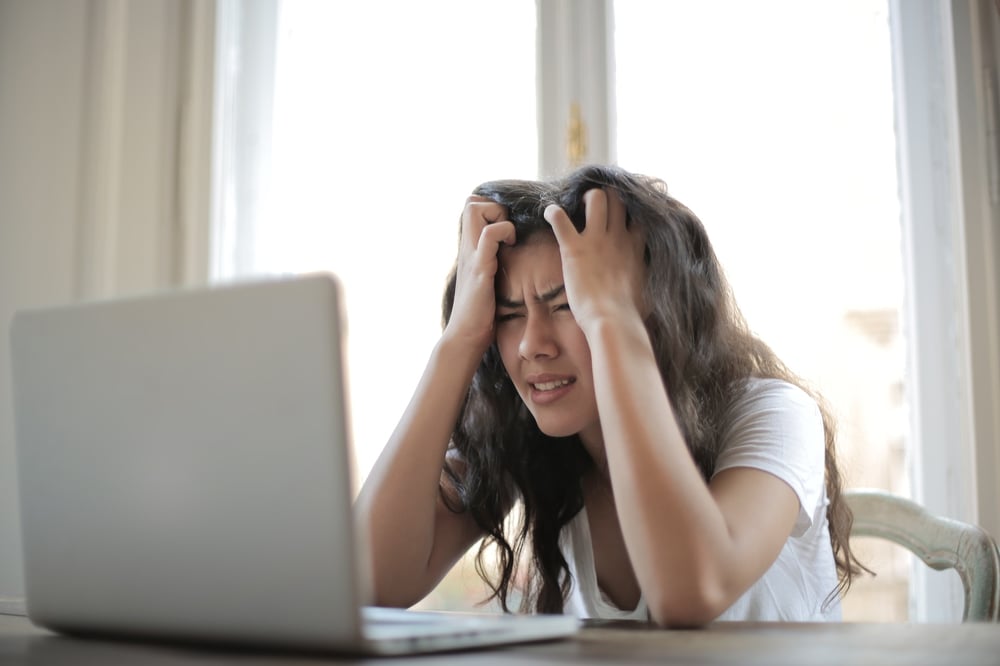A stressed writer clutching their head and staring at a computer screen.