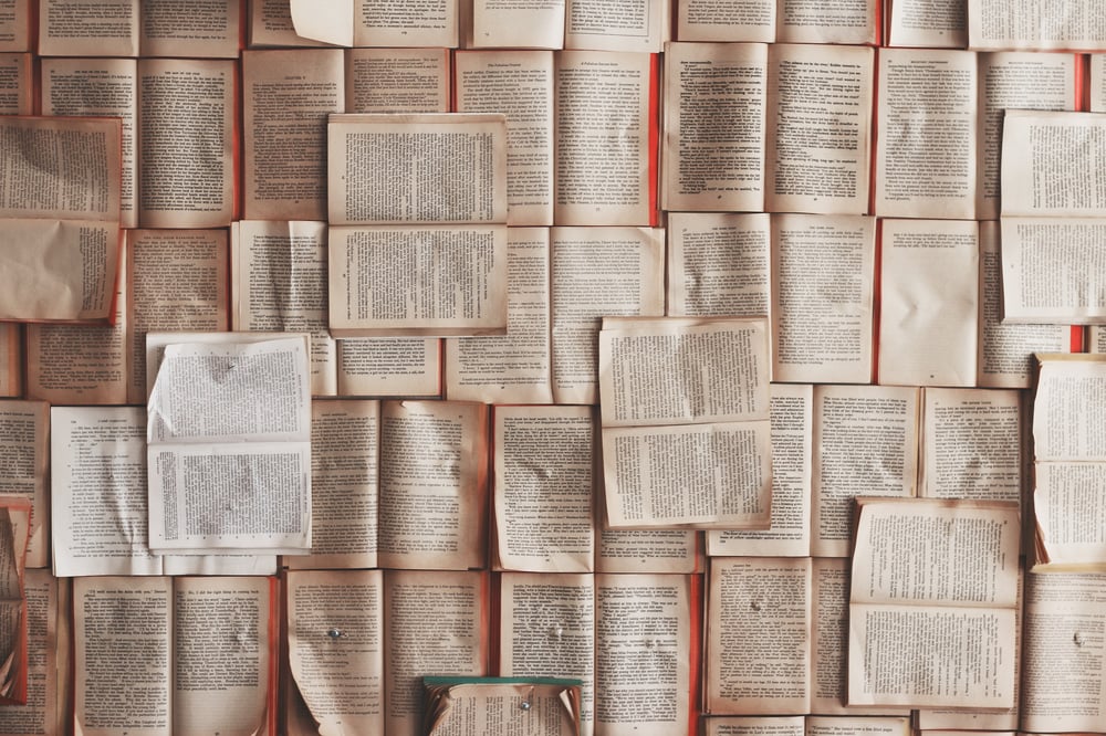 Dozens of paperback books pinned open against a barely visible orange background.