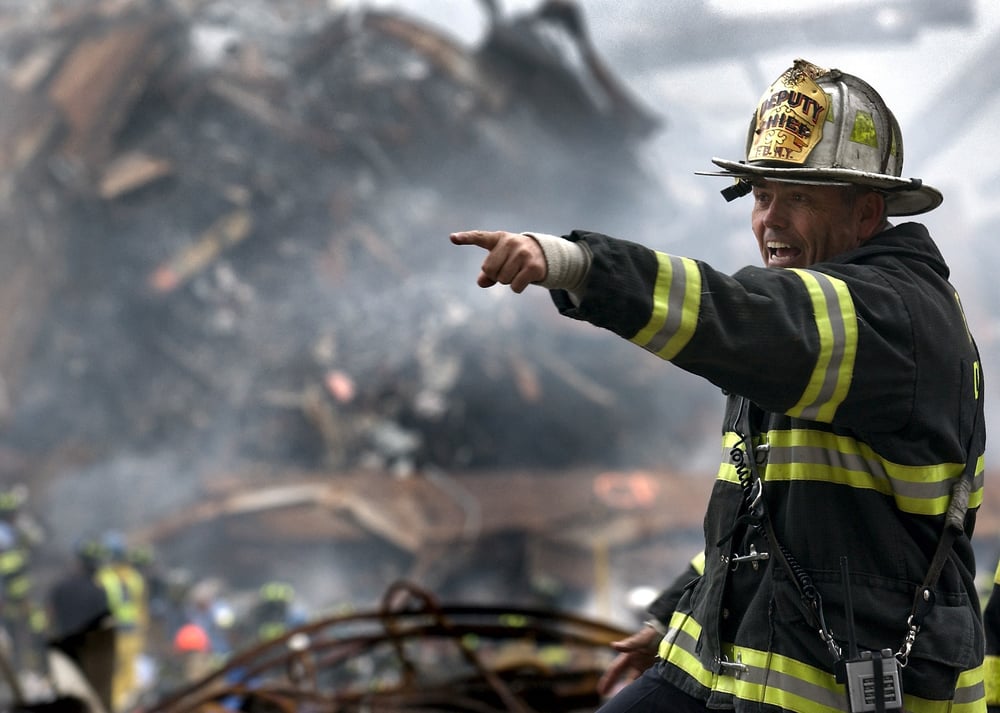 A firefighter points and yells in front of burned down rubble.