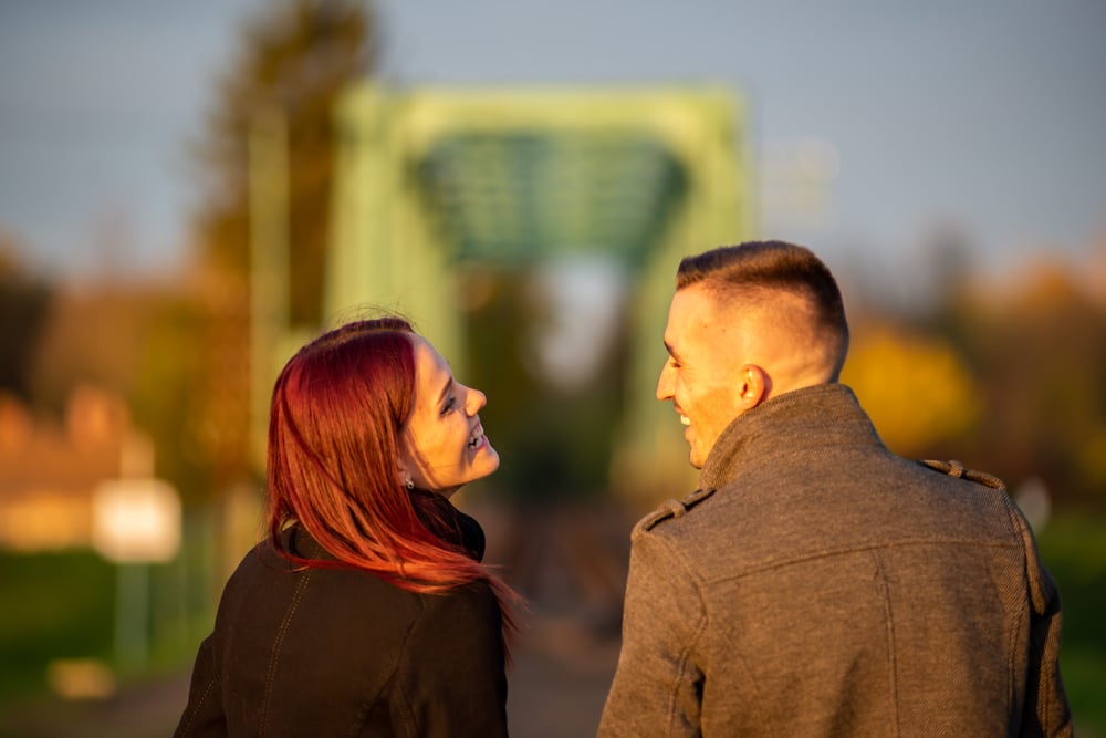 Two people laughing together as they walk towards a green bridge.