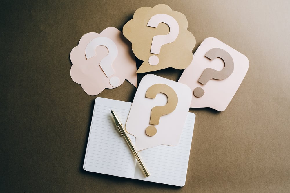 Brown, blush, and cream paper question marks arranged over an open notebook.