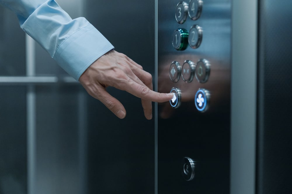 A hand presses a button on an elevator.
