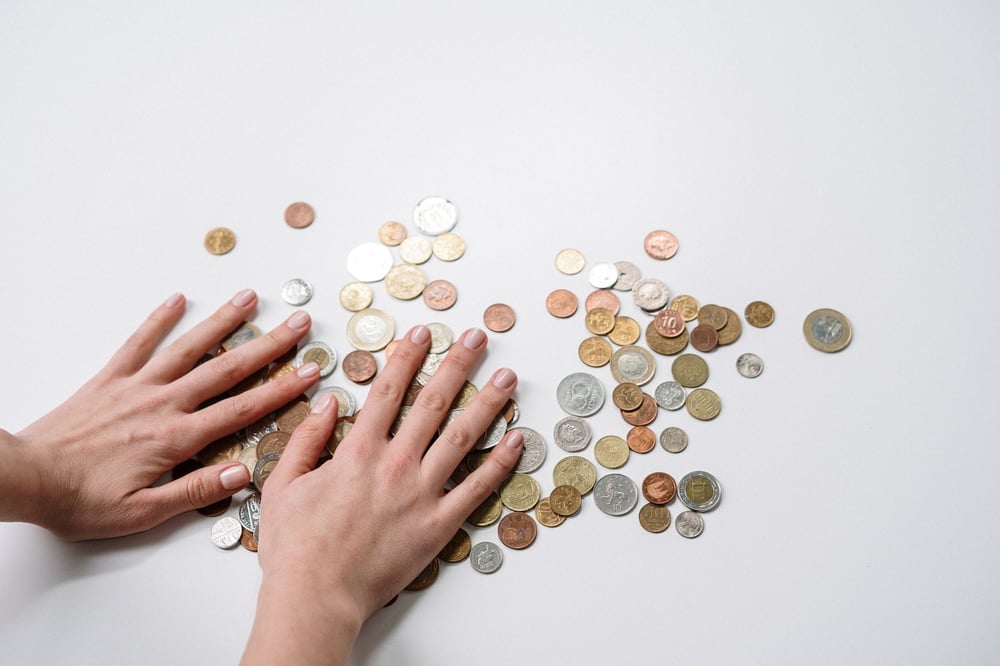 A pair of hands on op of coins scattered on a white background.