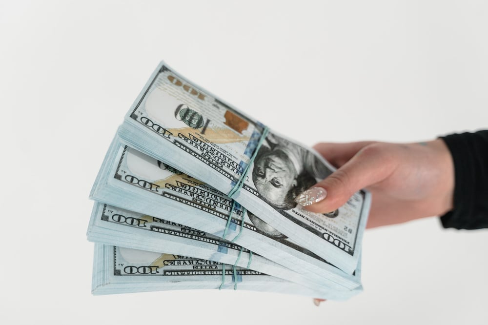 A hand holding stacks of $100 bills.