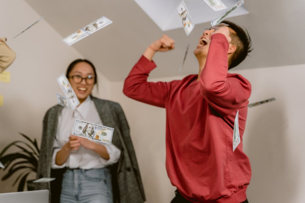 Two people celebrate while money falls from above them.