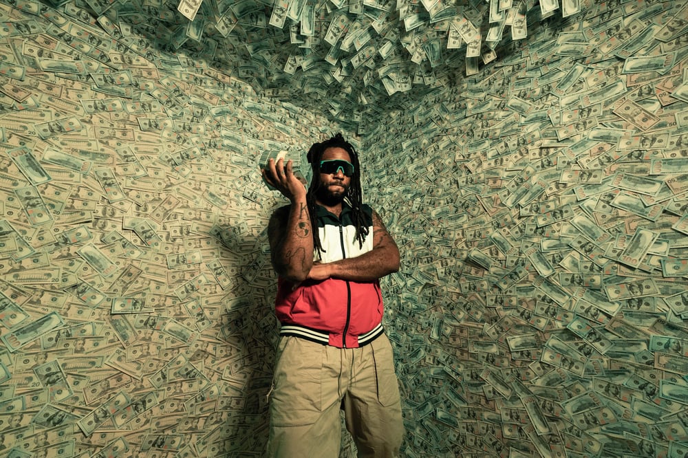 A person holds a stack of money inside a room where money covers the wall and ceiling.