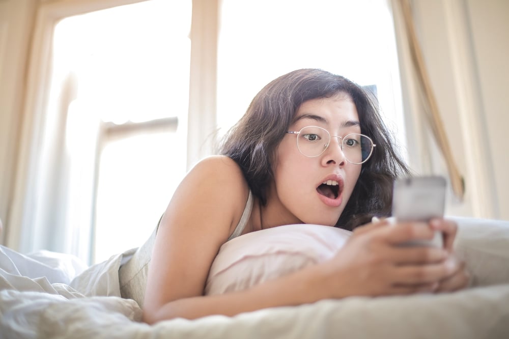 A female-presenting person looks at a phone screen with a shocked expression.