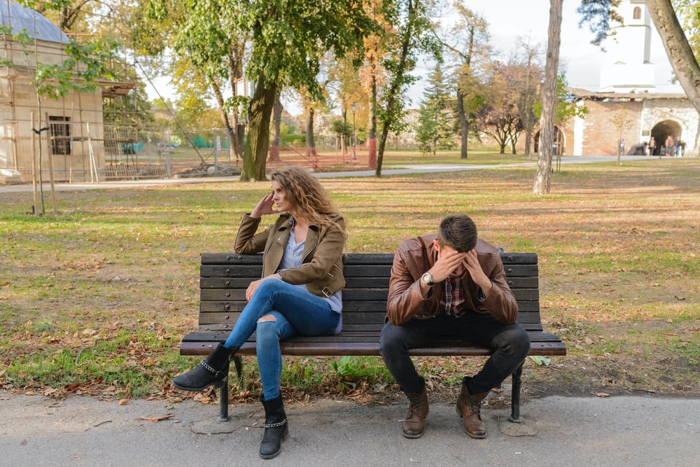 A couple sits on a bench turned away from each other after an argument.