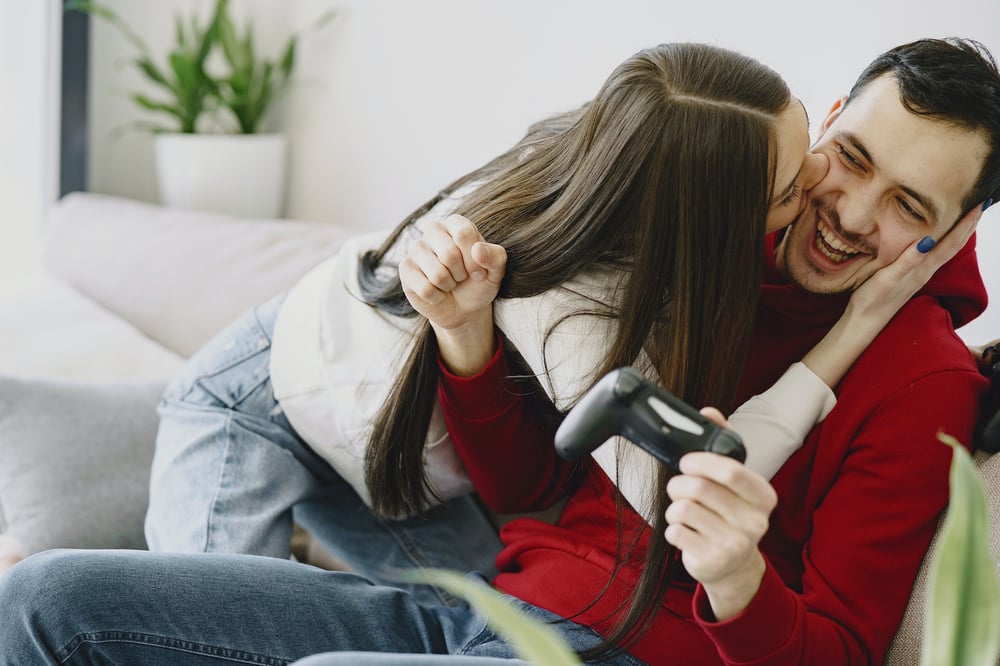 A woman kisses her boyfriend while he plays a video game.