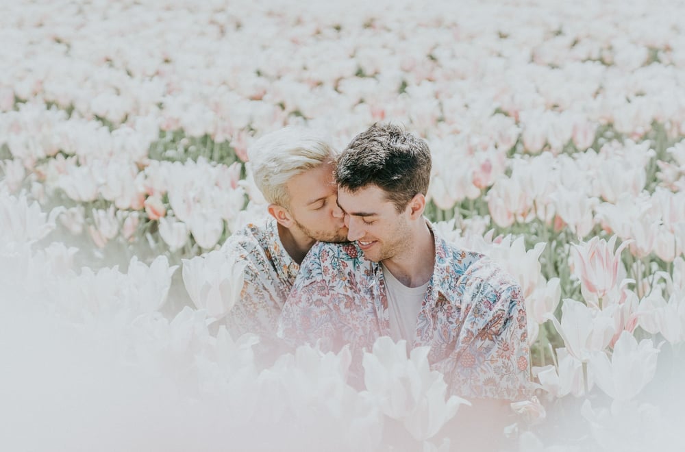 A couple kisses in a field of pink flowers.