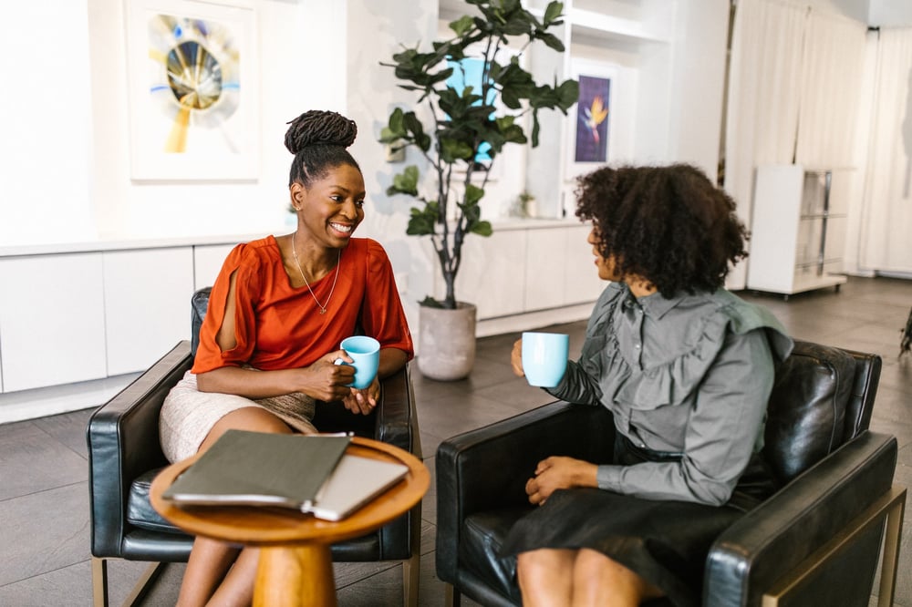 Two professionals smile while talking over coffee.