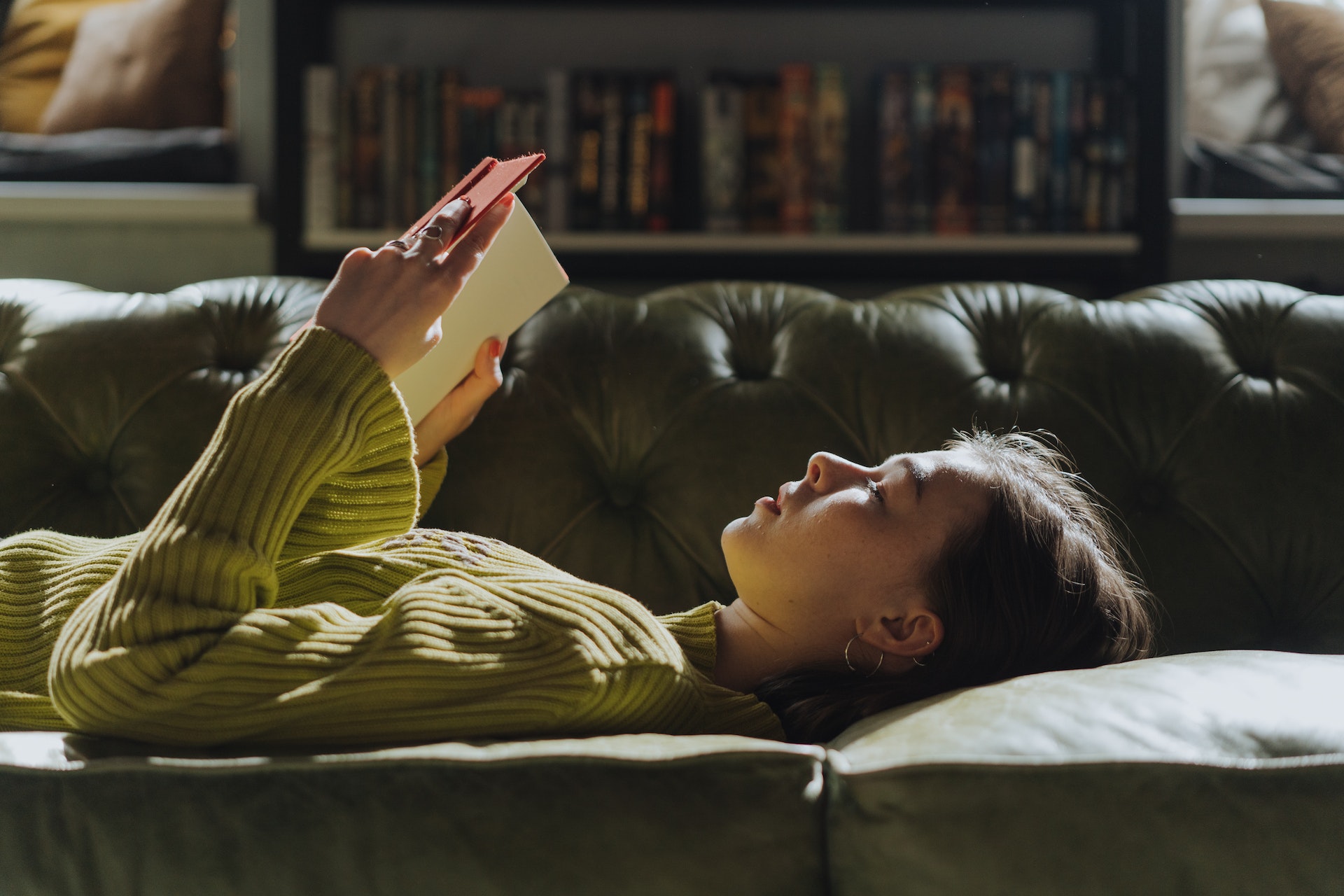A person lies on a coach reading a book.