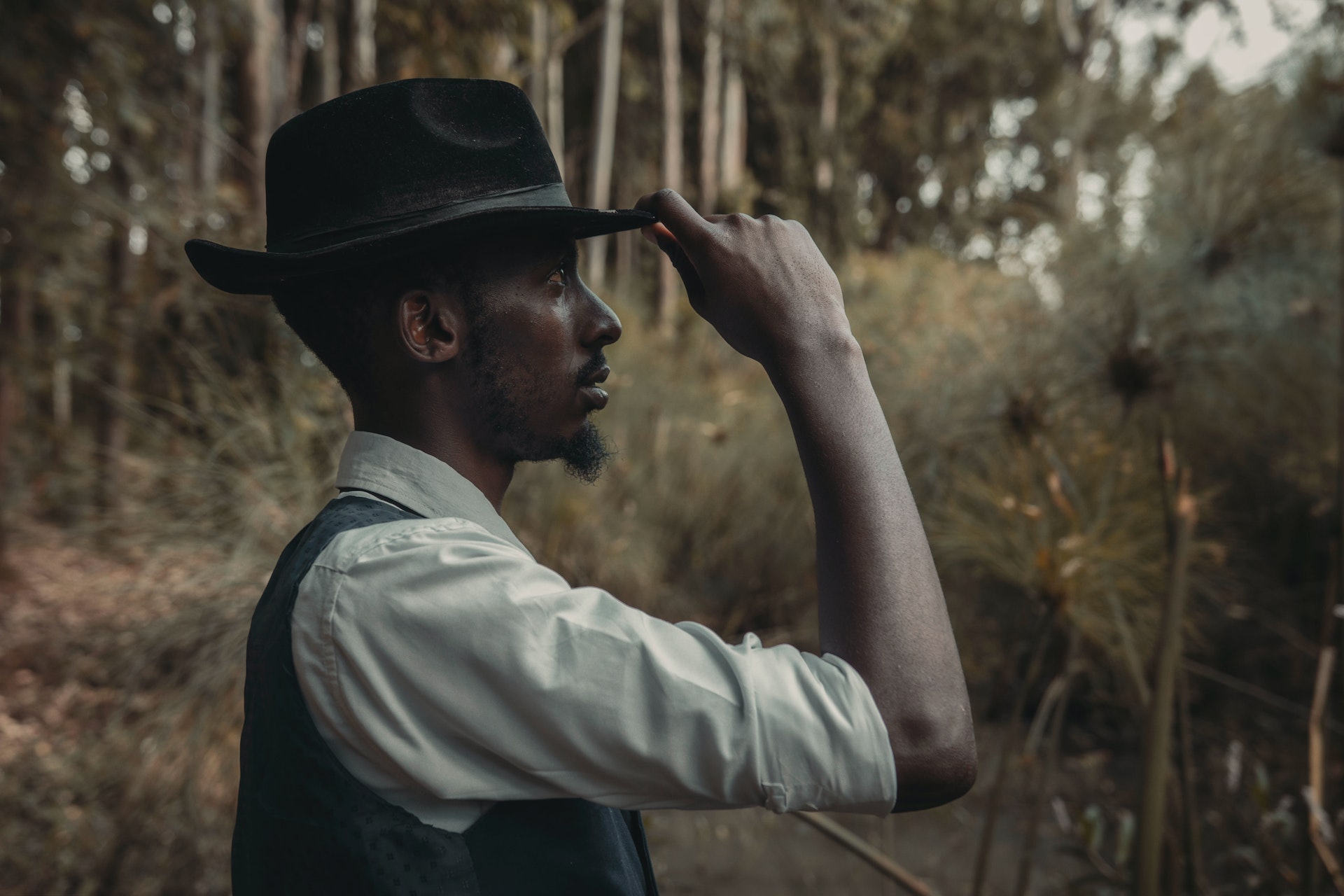 A person from the old west touches his hat as he looks into the distance.